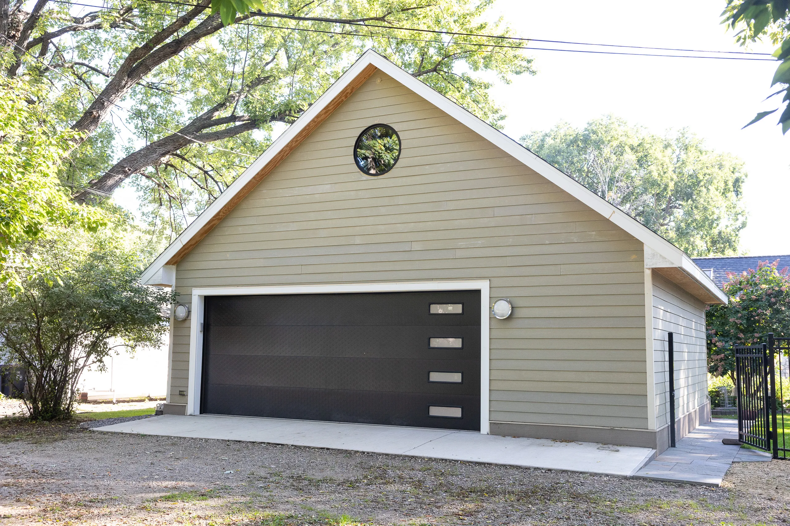 Modern detached garage with gray siding, black overhead door and round gable window