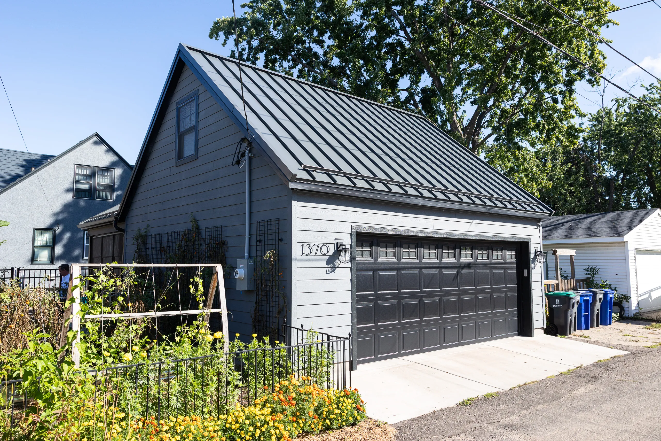 Custom detached garage with gray siding, black overhead door and standing-seam metal roof