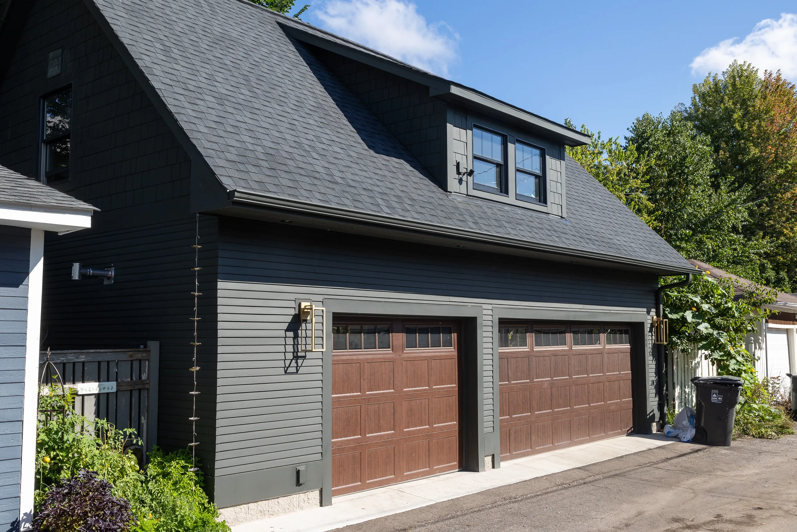 Custom three-car detached garage with dark siding, wood-look doors and upper dormer windows