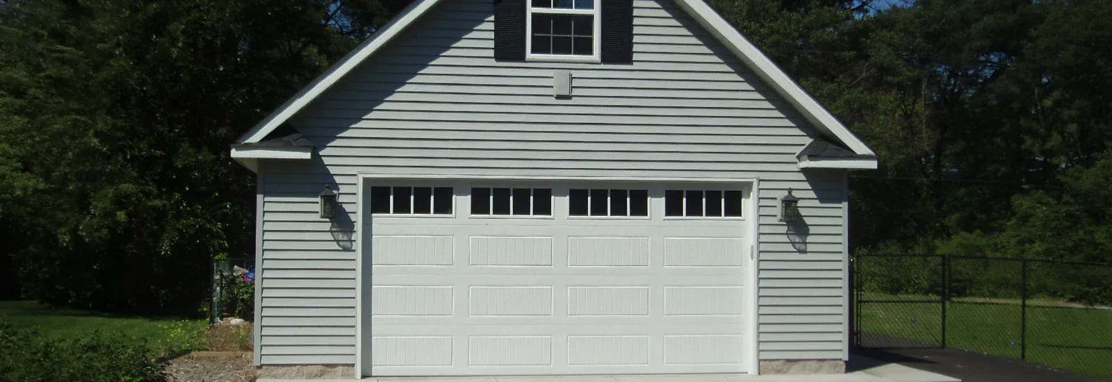 Custom two-car detached garage with gray siding, carriage-style door and upper storage window
