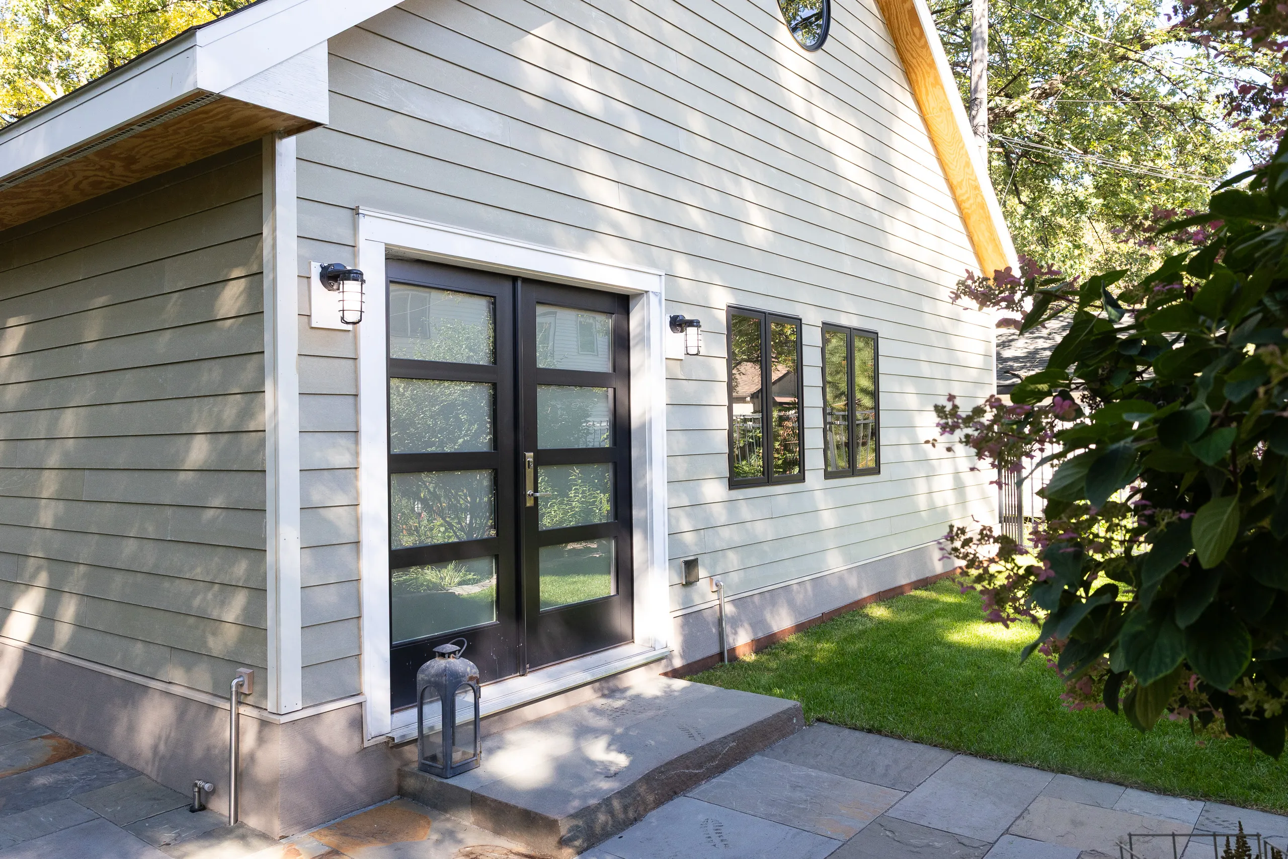 Custom three-car detached garage with dark siding, wood-look doors and upper dormer windows