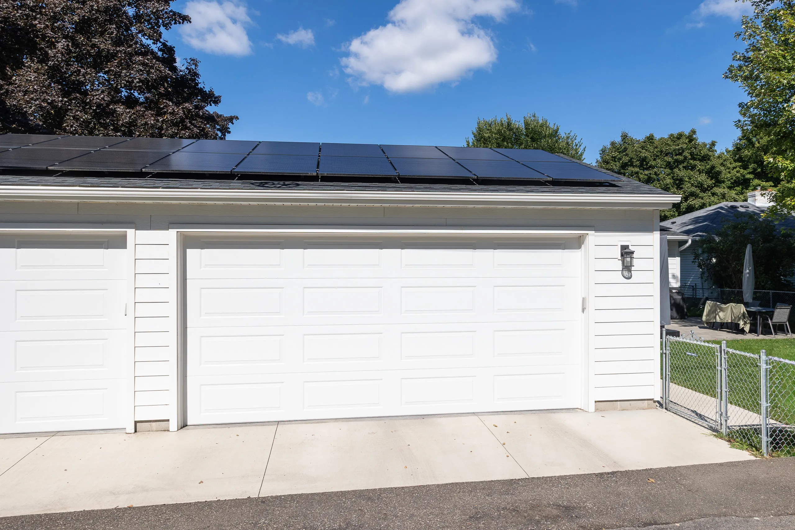 Custom three-car detached garage with white doors, gray siding and rooftop solar panels