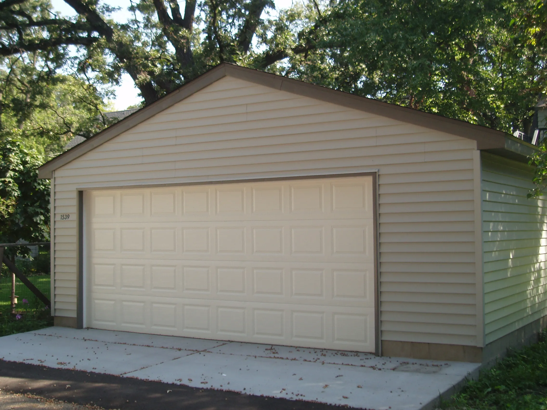 Detached two-car garage with white vinyl siding, paneled overhead door and concrete apron