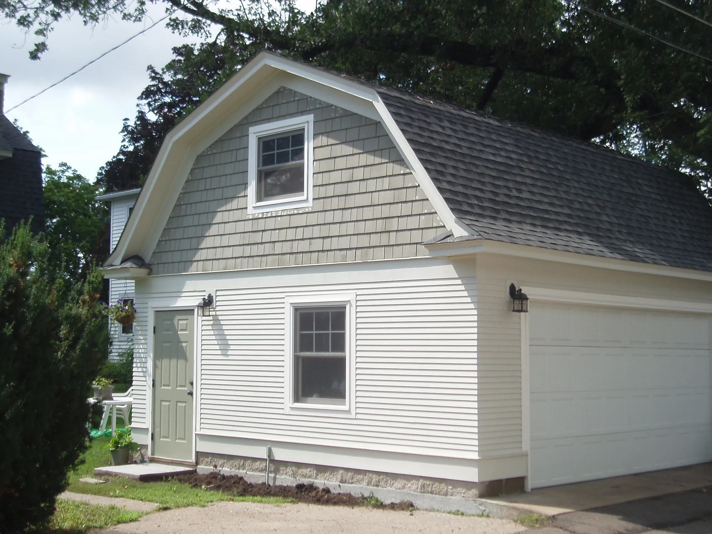 Custom gambrel-roof detached garage with white siding, side entry door and upper-level windows