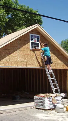 Garage under construction with a carpenter installing an upper gable window