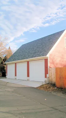 Large red detached three-car garage with white doors and a steep gable roof