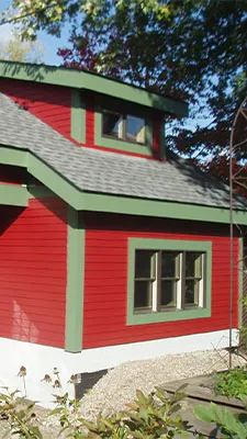 Red custom garage exterior with green trim, side windows and a roof dormer