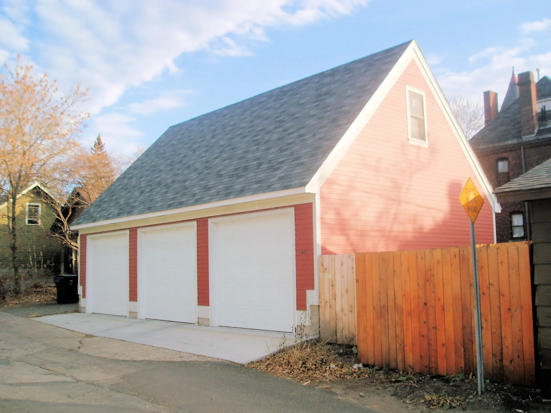 Red three-car detached garage with separate white overhead doors and steep gable roof